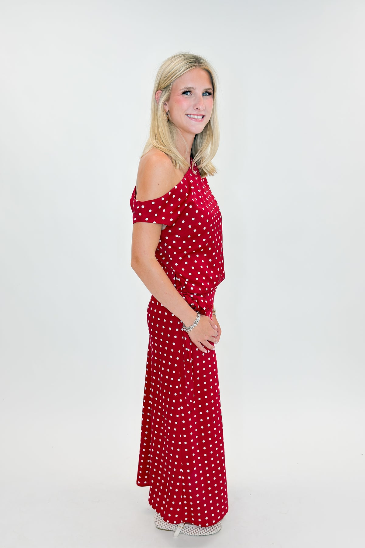 Side view of woman wearing Swagger Boutique’s Red &amp; White Polka Dot Midi Skirt with Red &amp; White Polka Dot Asymmetrical Tank against white studio background.