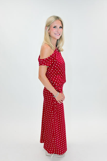 Side view of woman wearing Swagger Boutique’s Red &amp; White Polka Dot Midi Skirt with Red &amp; White Polka Dot Asymmetrical Tank against white studio background.