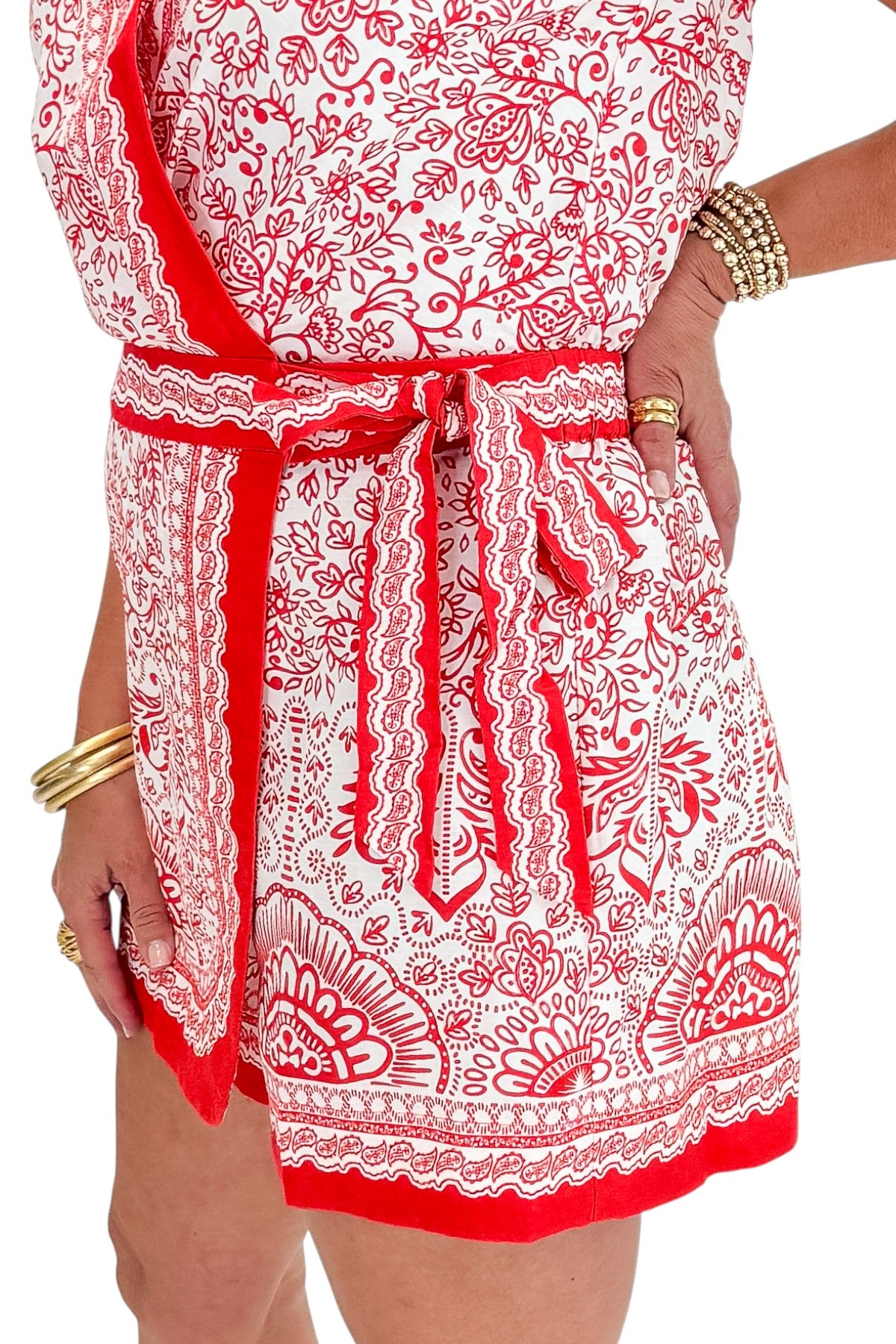 Side detail view of woman wearing Swagger Boutique’s Red &amp; White Printed Romper by Skies Are Blue with sandals against white studio background.