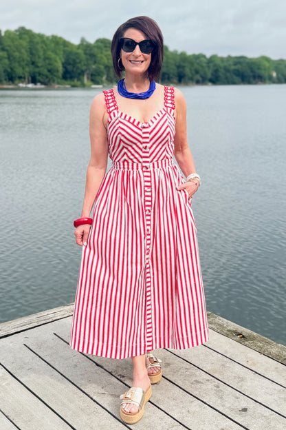 Front view of woman wearing Swagger Boutique’s Red, White &amp; Blue Striped Midi Dress with sandals standing outside at the lake.