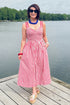 Front view of woman wearing Swagger Boutique’s Red, White & Blue Striped Midi Dress with sandals standing outside at the lake.