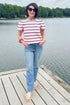 Front view of woman wearing Swagger Boutique’s Red, White & Blue Striped Top by Entro with jeans standing on a dock outside.