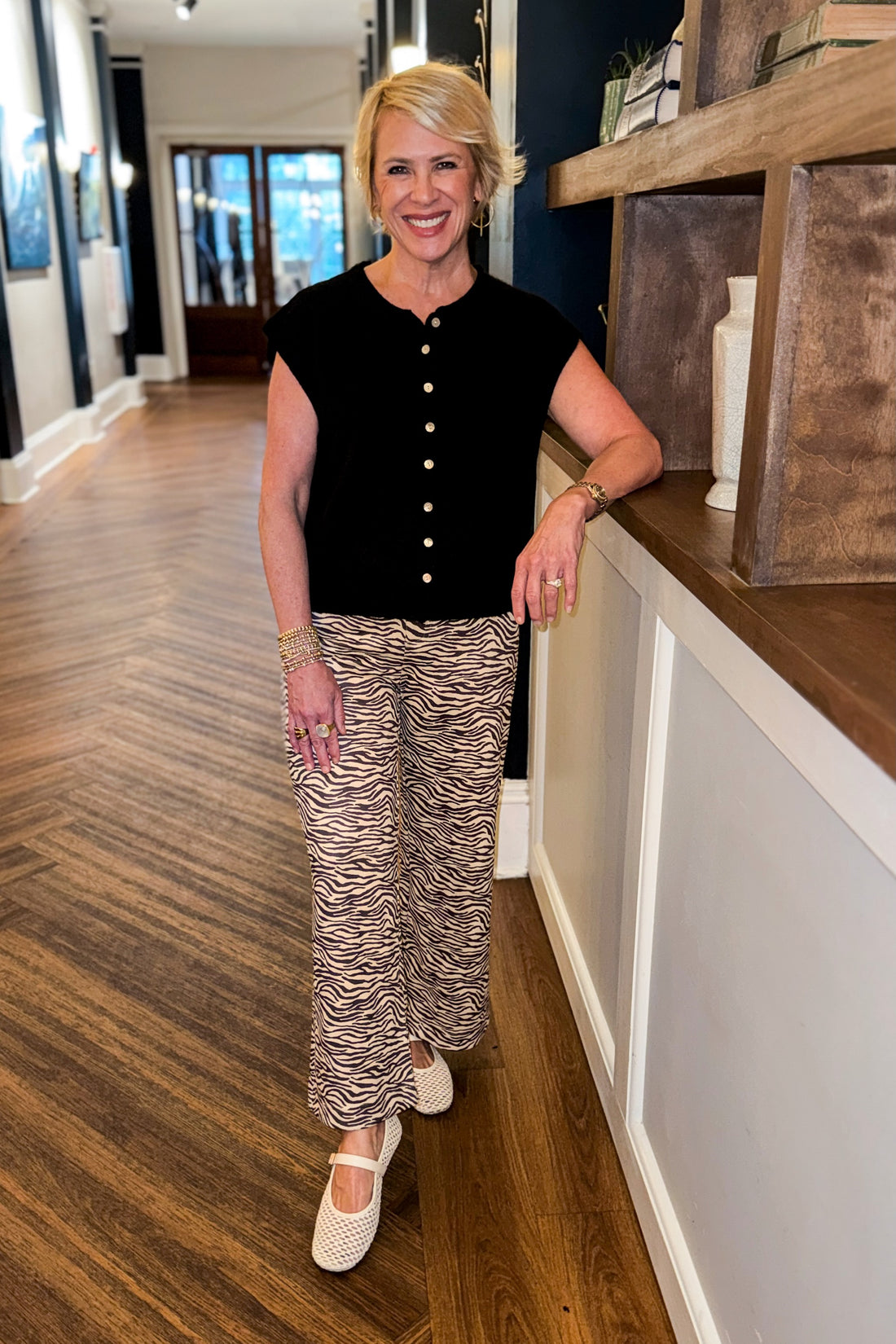 Front view of woman wearing Swagger Boutique’s Zebra Print Suede Pants with Black Sweater standing at an Art Gallery. 