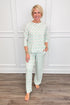 Model wearing the Rosy Woodlands Annie Pajama Set, featuring an allover green Christmas tree print with pink bows on a white background. The set includes a relaxed-fit, long-sleeve crewneck top and matching straight-leg pajama pants with side pockets.