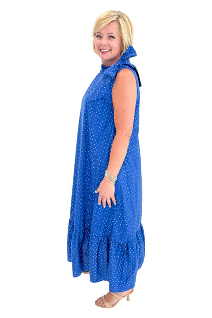 Side view of woman wearing Swagger Boutique’s Royal Blue Polka Dot Tue Neck Midi Dress against white studio background.
