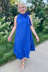 Front view of woman wearing Swagger Boutique’s Royal Blue Polka Dot Tue Neck Midi Dress walking outside on a path.