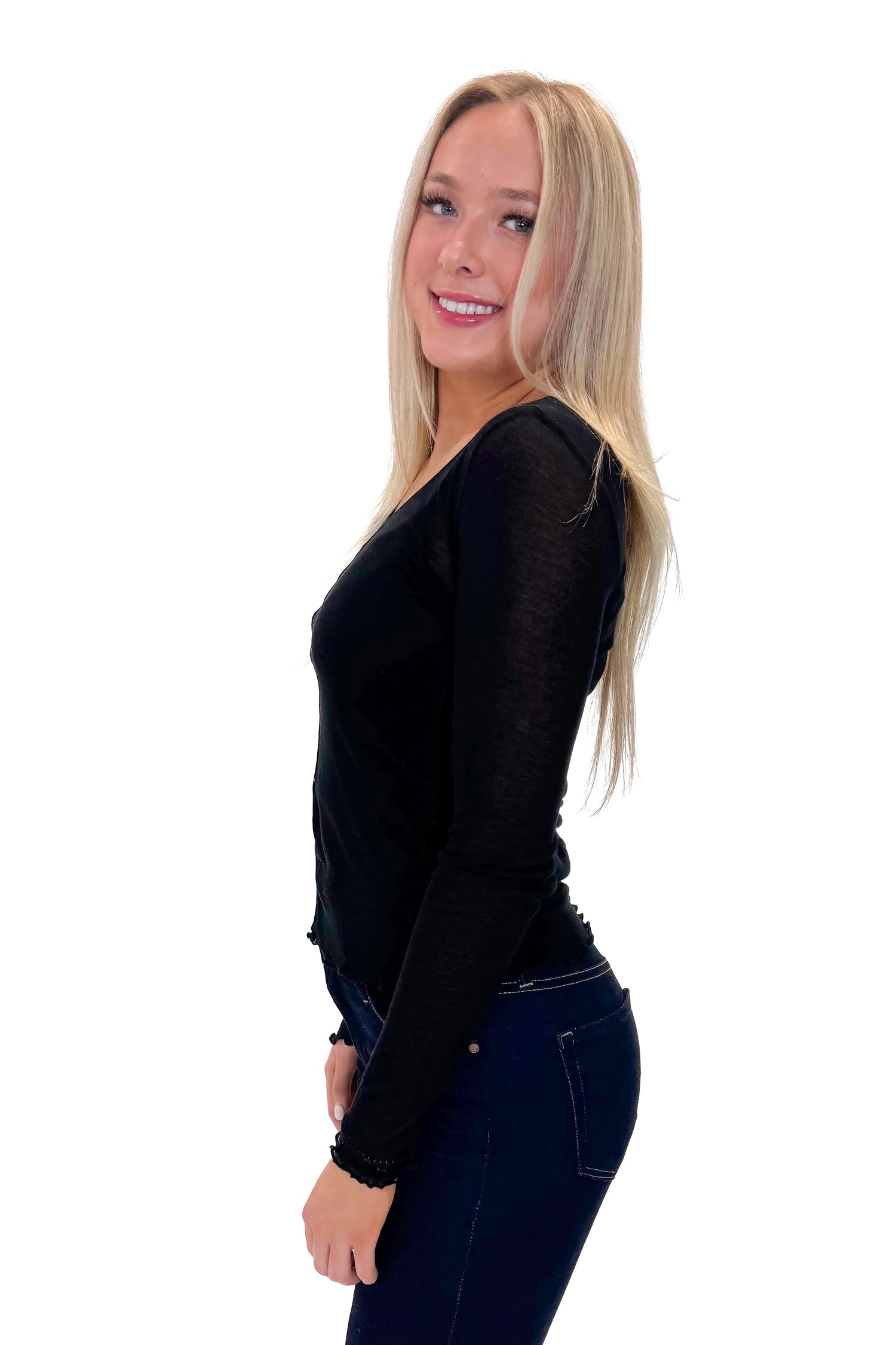 Side view of woman wearing Black Sheer Long Sleeve Top with jeans against white studio background.