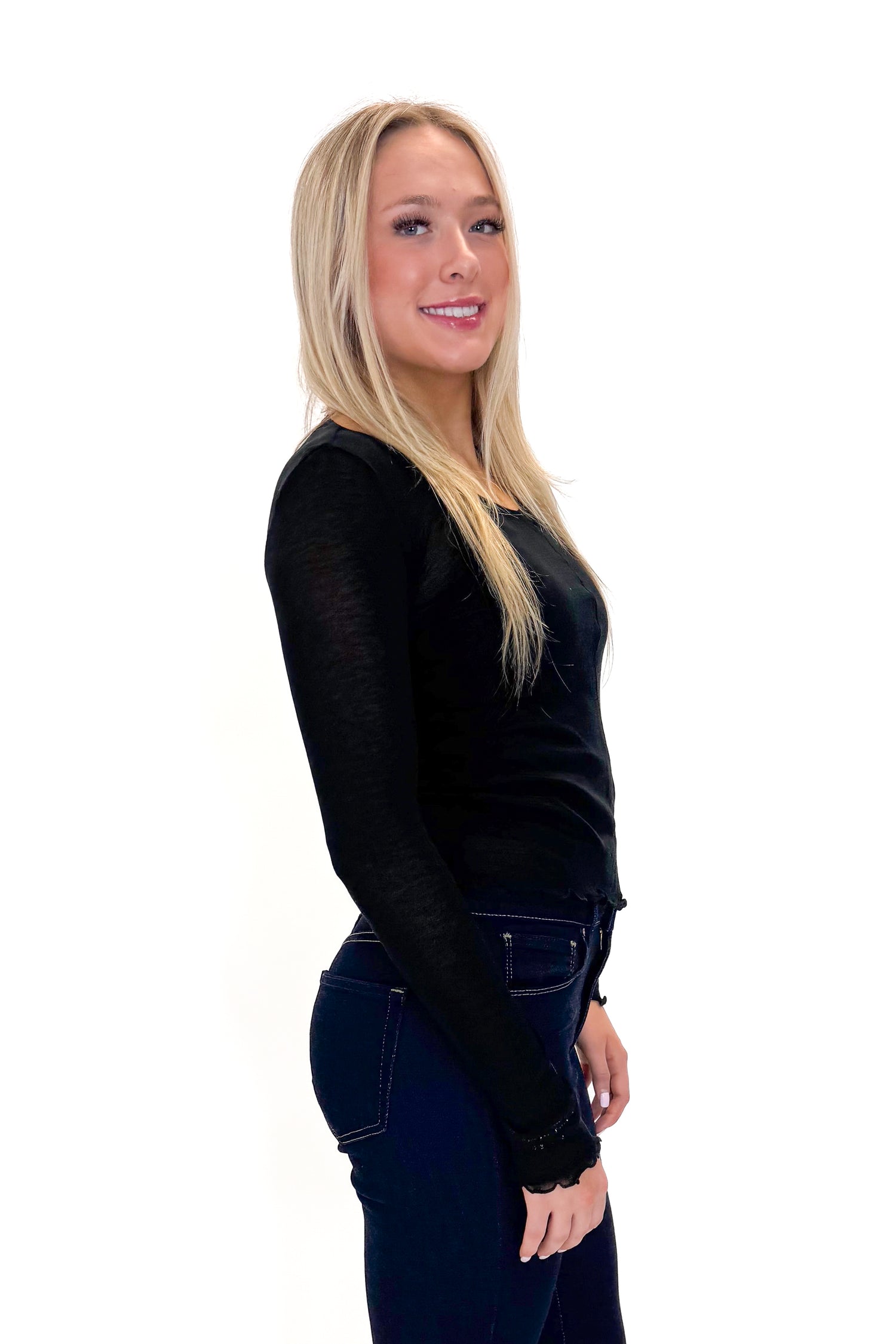 Side view of woman wearing Black Sheer Long Sleeve Top with jeans against white studio background.