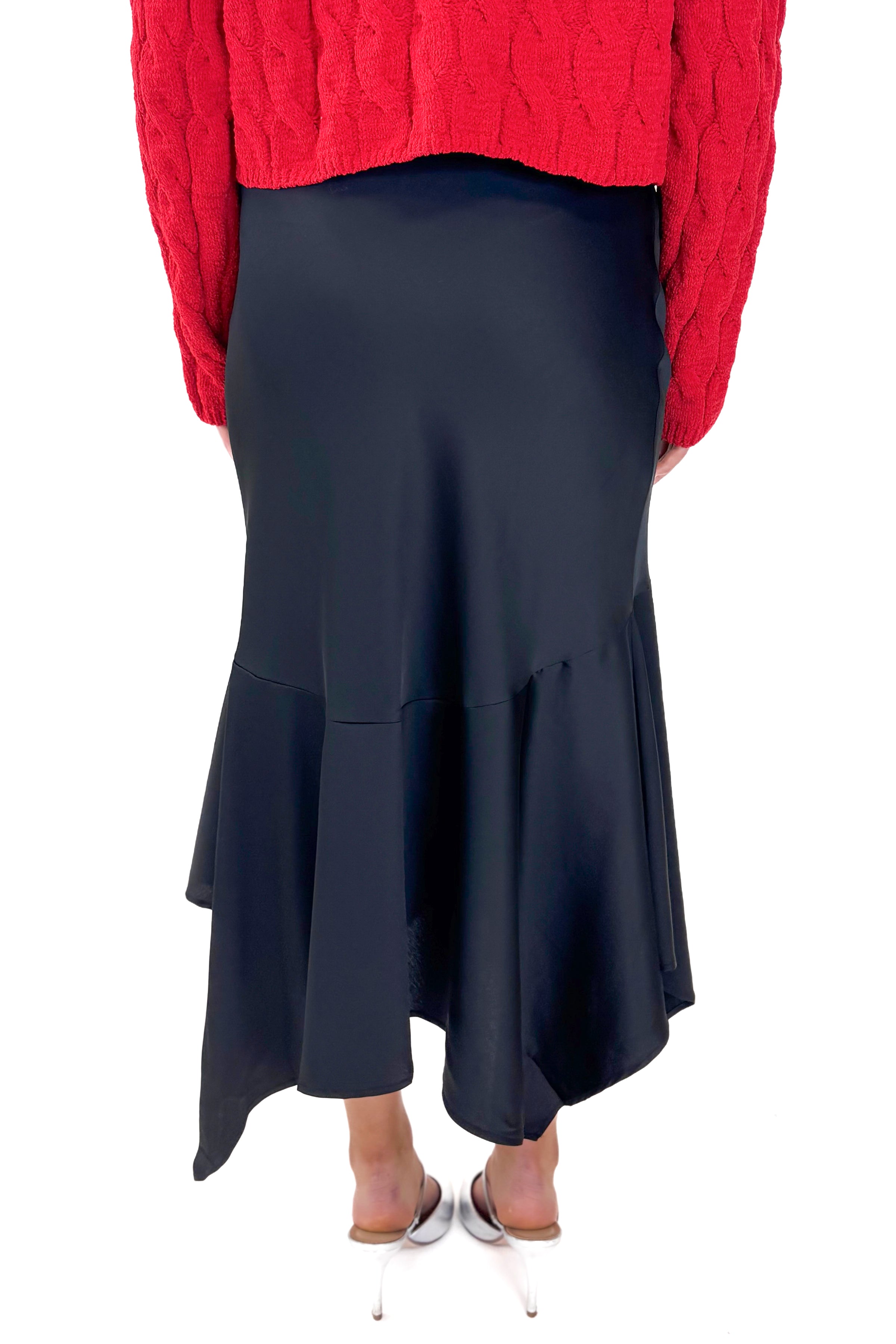 Back view of woman wearing Black Satin Handkerchief Hem Midi Skirt with sweater against white studio background.