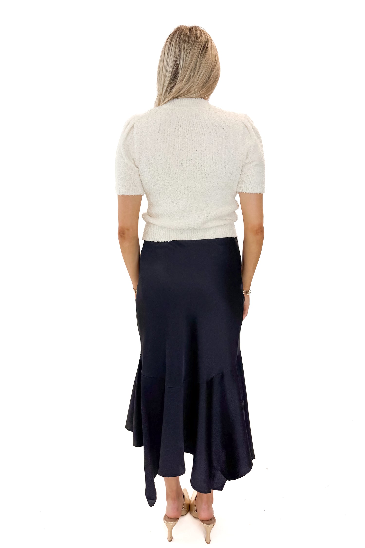 Back view of woman wearing Black Satin Handkerchief Hem Midi Skirt with sweater against white studio background.