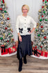 Front view of woman wearing Black Satin Handkerchief Hem Midi Skirt with sweater against holiday decor.