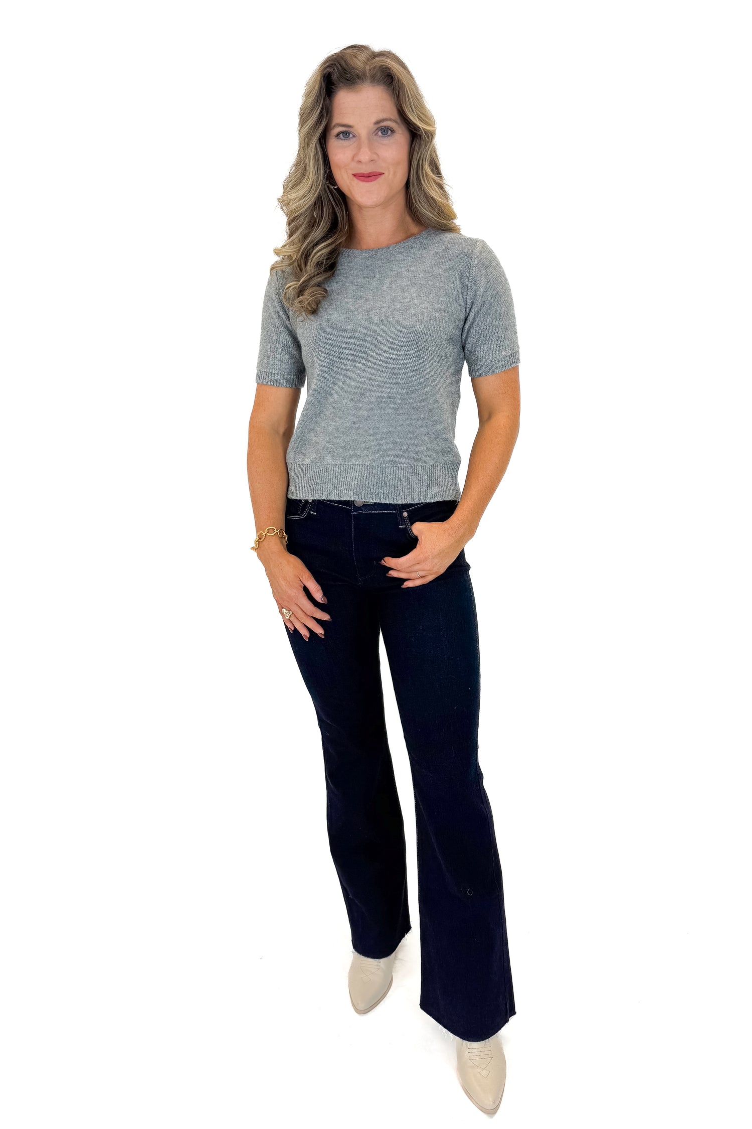Front view of woman wearing Grey Short Sleeve Crewneck Sweater with jeans against white studio background.