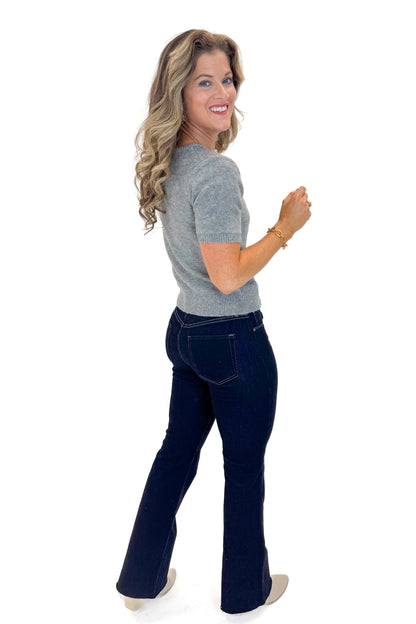 Side view of woman wearing Grey Short Sleeve Crewneck Sweater with jeans against white studio background.