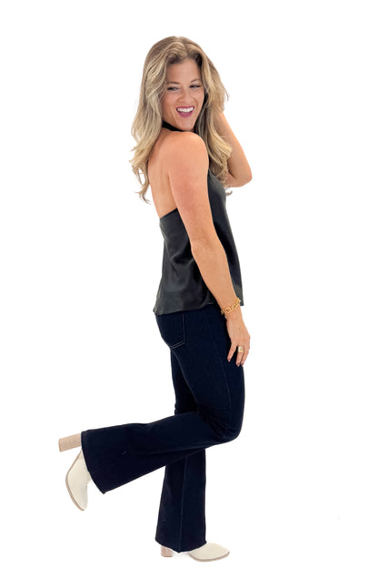 Side view of woman wearing Black Satin Halter Neck Top with jeans against white studio background.