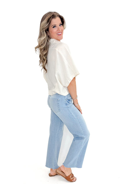 Side view of woman wearing Linen V-neck Collared Top with jeans against white studio background.
