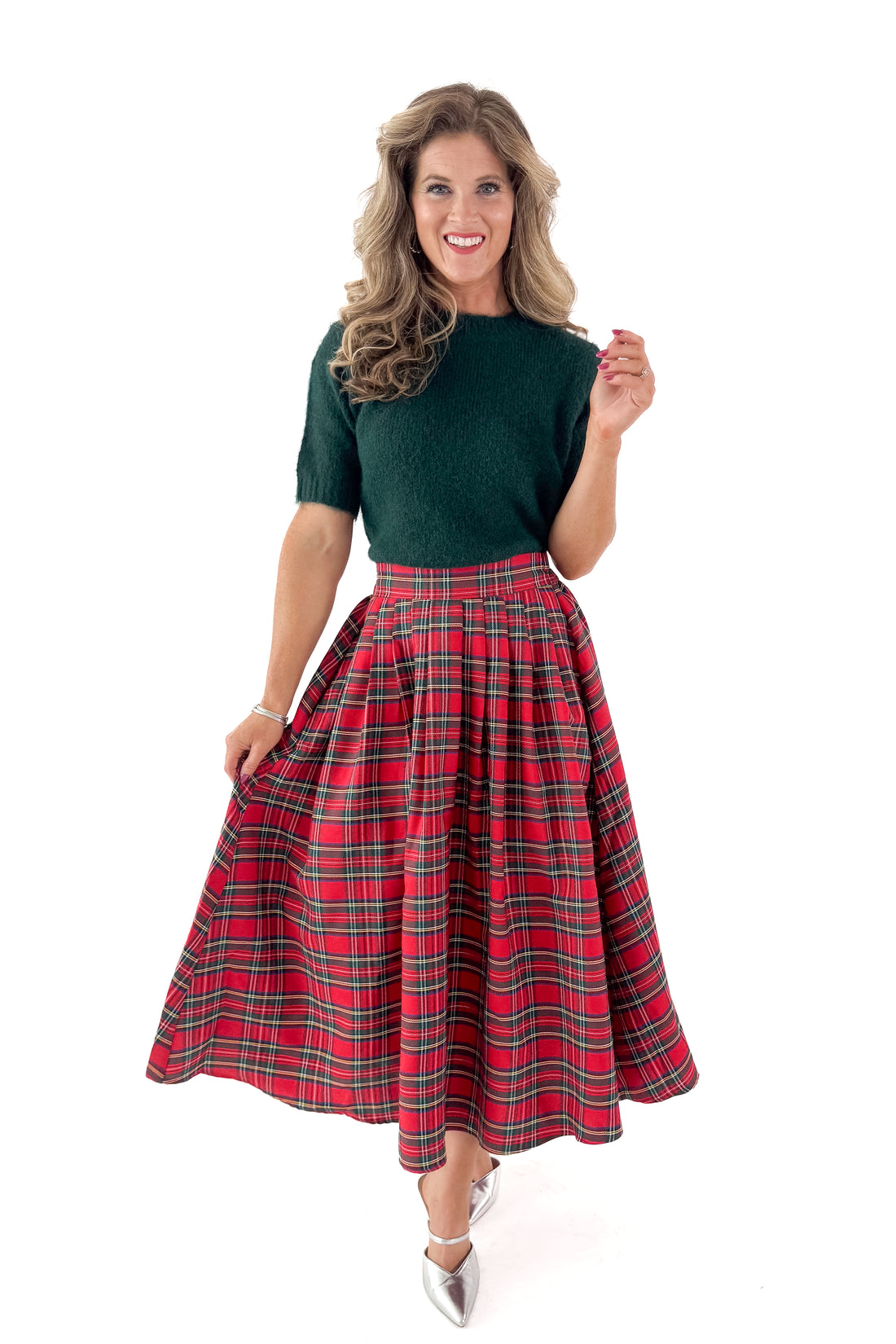 Front view of woman wearing green sweater with red tartan skirt against white studio background.