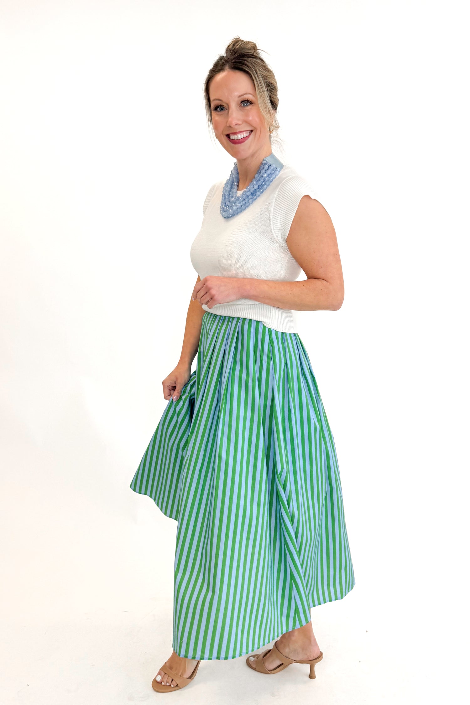 Side view of woman wearing Green &amp; Blue Striped Skirt by Entro with white sweater against white studio background.