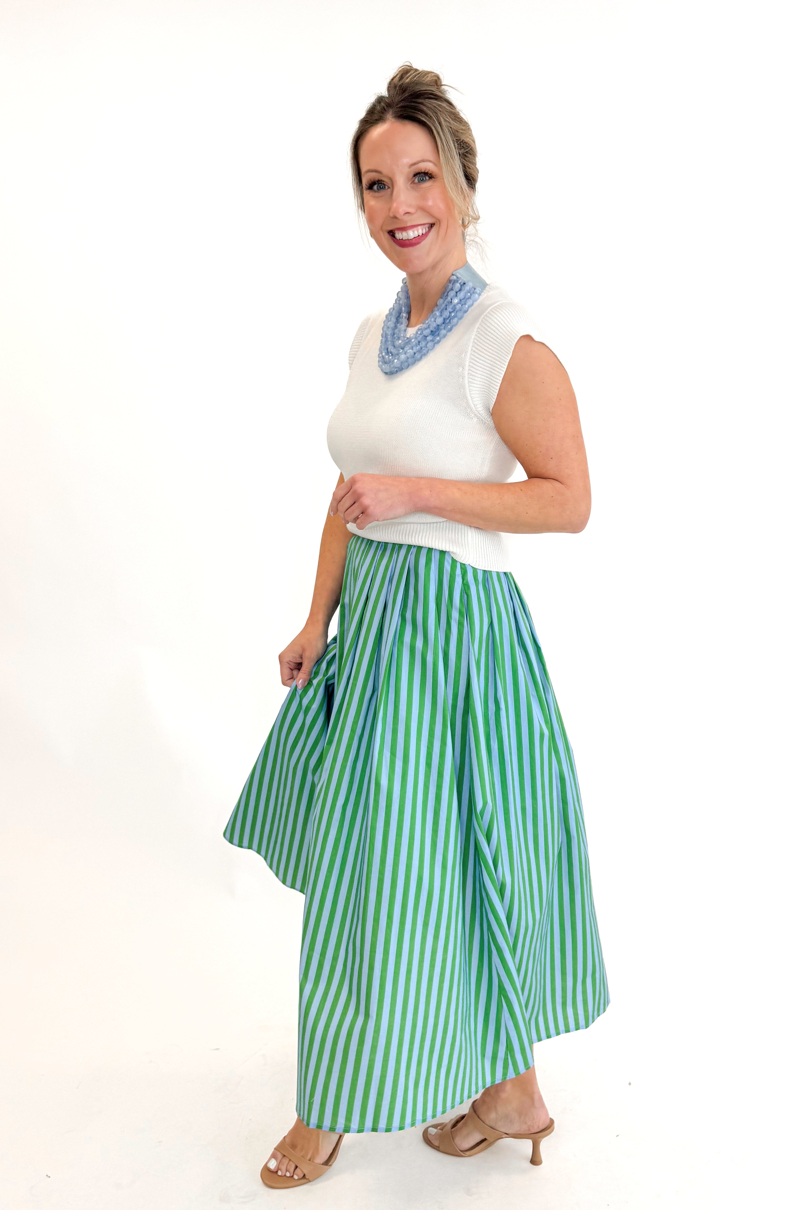 Side view of woman wearing Green &amp; Blue Striped Skirt by Entro with white sweater against white studio background.