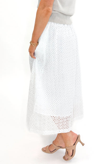 Side view of woman wearing Off White Eyelet Midi Skirt by Entro with sweater against white studio background.