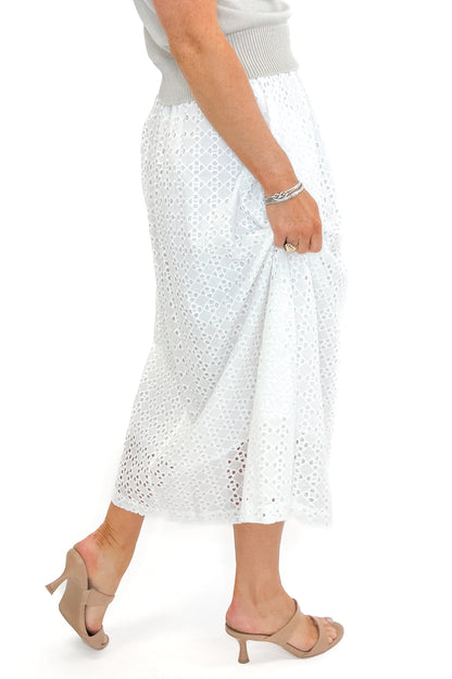 Side view of woman wearing Off White Eyelet Midi Skirt by Entro with sweater against white studio background.