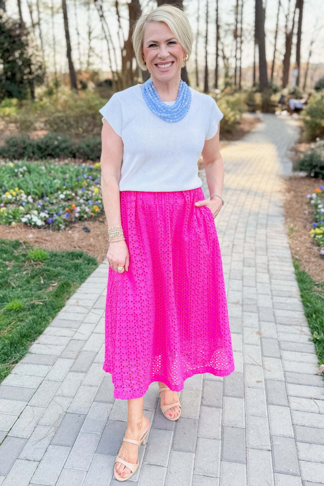 Front view of woman wearing white sweater with Hot Pink Eyelet Midi Skirt by Entro at a garden outside.