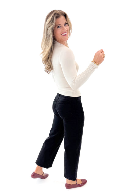 Side view of woman wearing Cream Ribbed Mock Neck Top with jeans against white studio background.