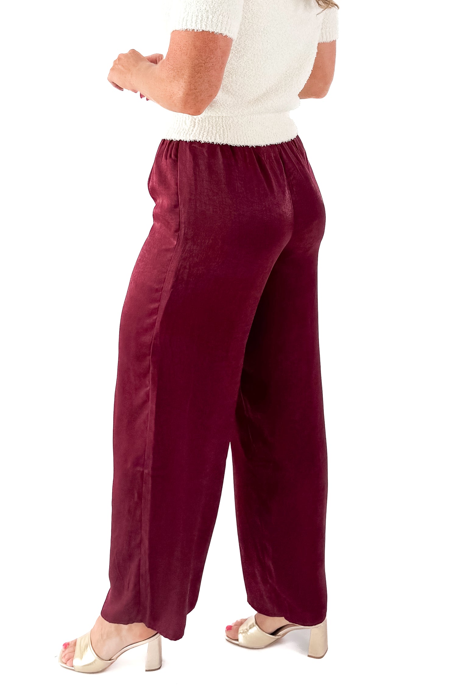 Side view of woman wearing cream sweater and Wine Satin Wide Leg Pants against white studio background.