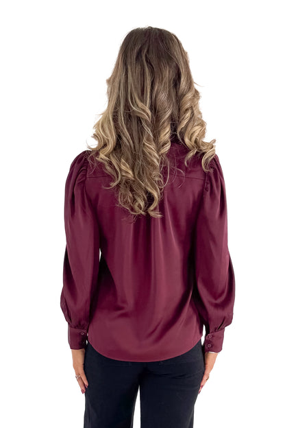 Back view of woman wearing Plum Satin Button Up Top with jeans against white studio background.