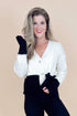 Woman wearing a white cardigan over a black outfit against a beige background