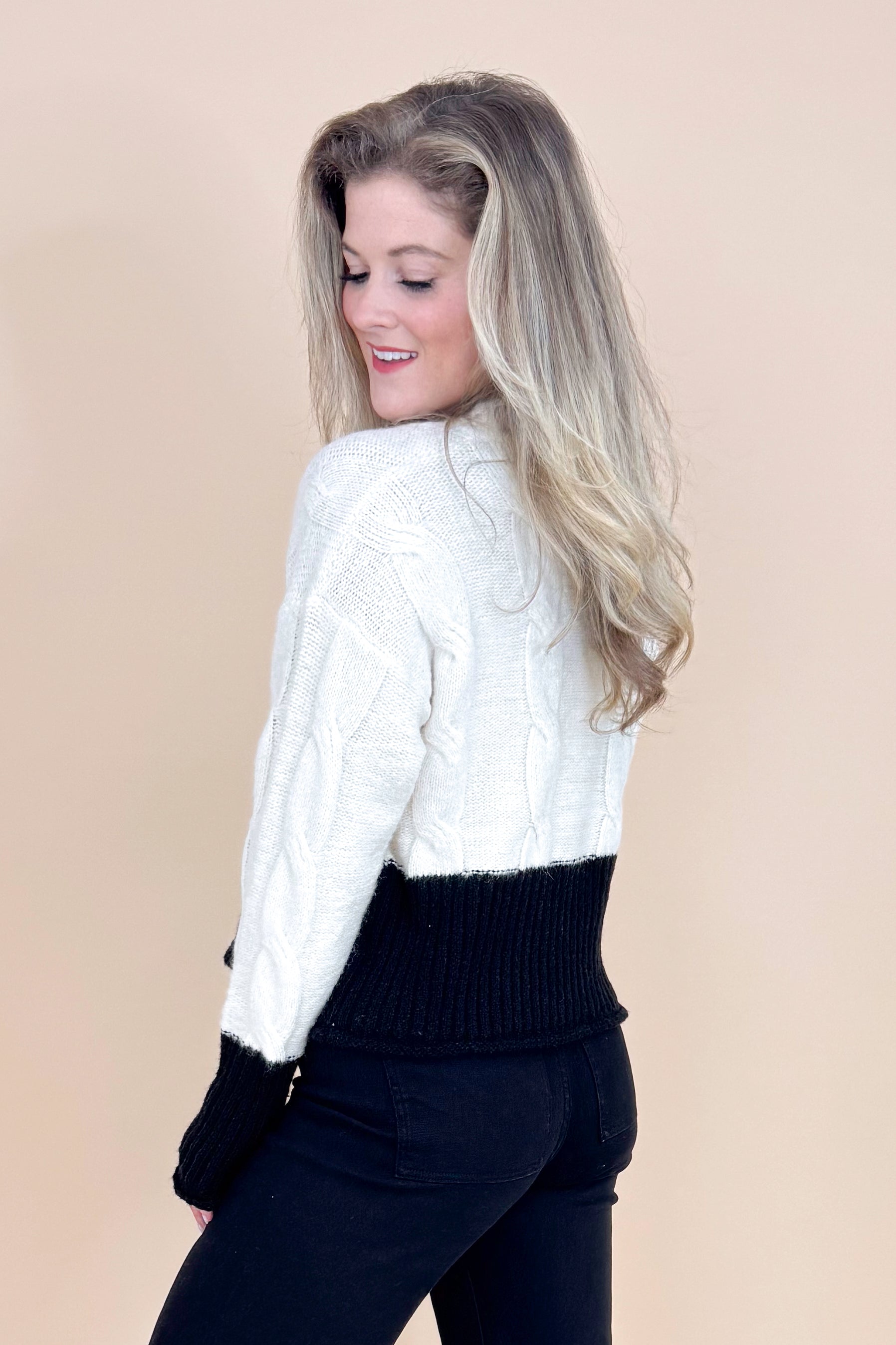 Woman wearing a white and black cable knit sweater on a beige background
