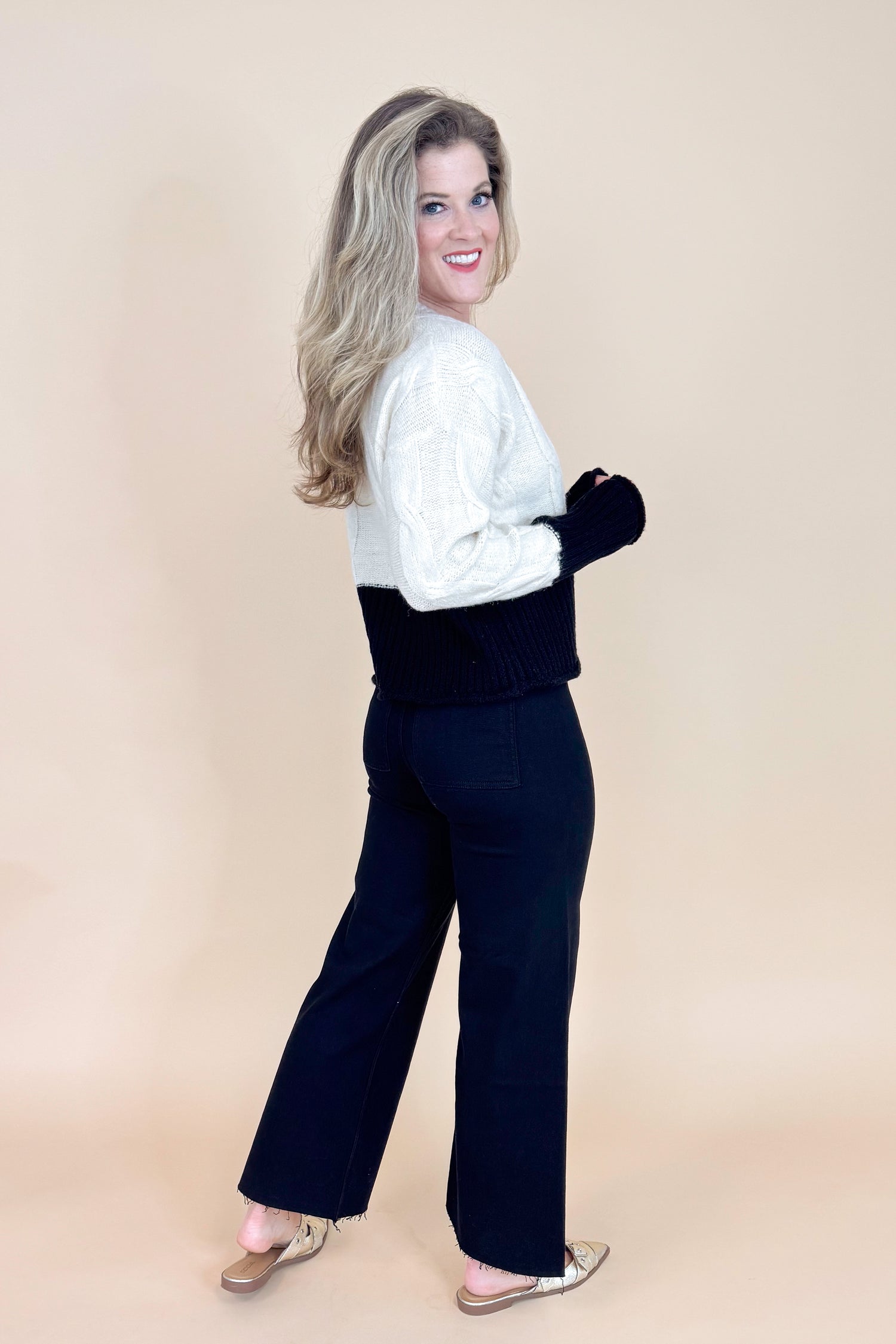 Woman wearing a white sweater and black pants on a beige background