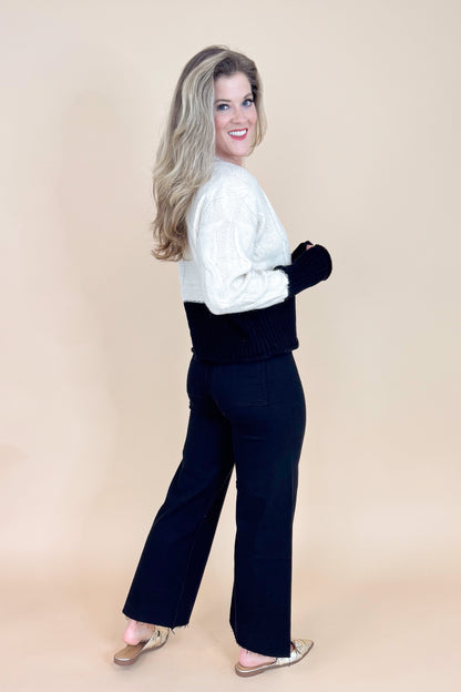 Woman wearing a white sweater and black pants on a beige background