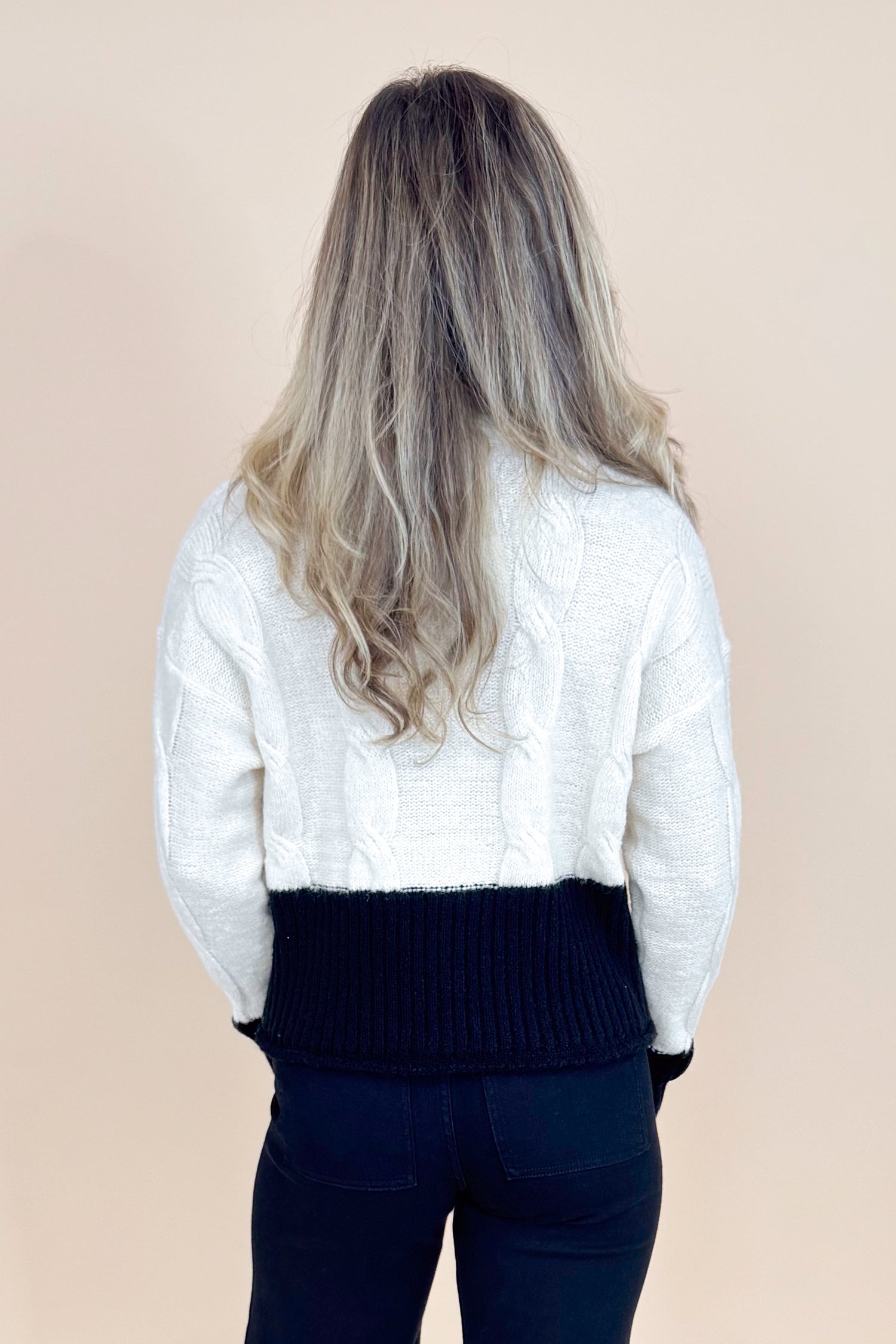 Person wearing a white sweater with black accents on a beige background