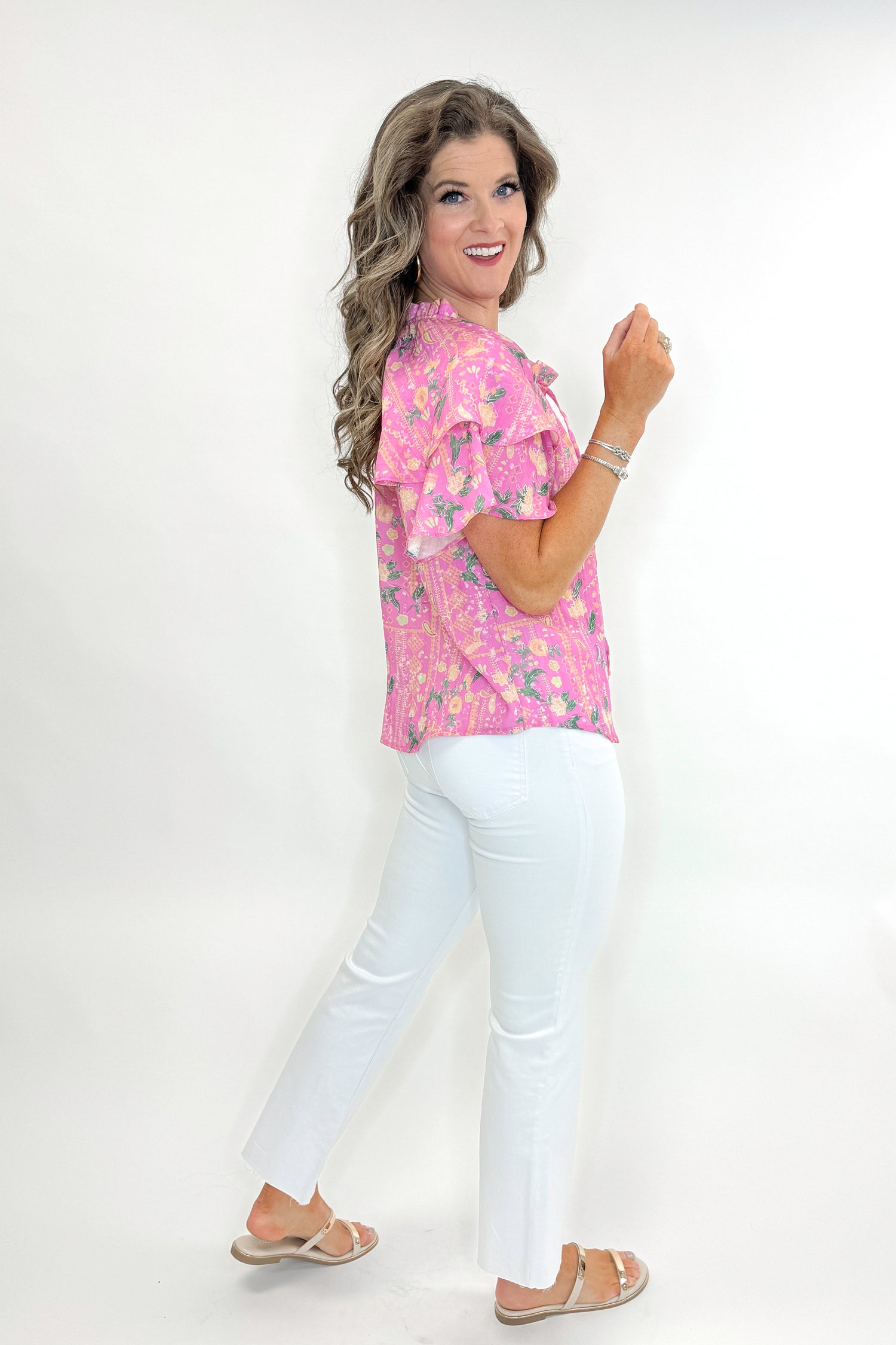 Sid view of woman wearing Pink Floral Printed Ruffle Sleeve Top with jeans against white studio background.
