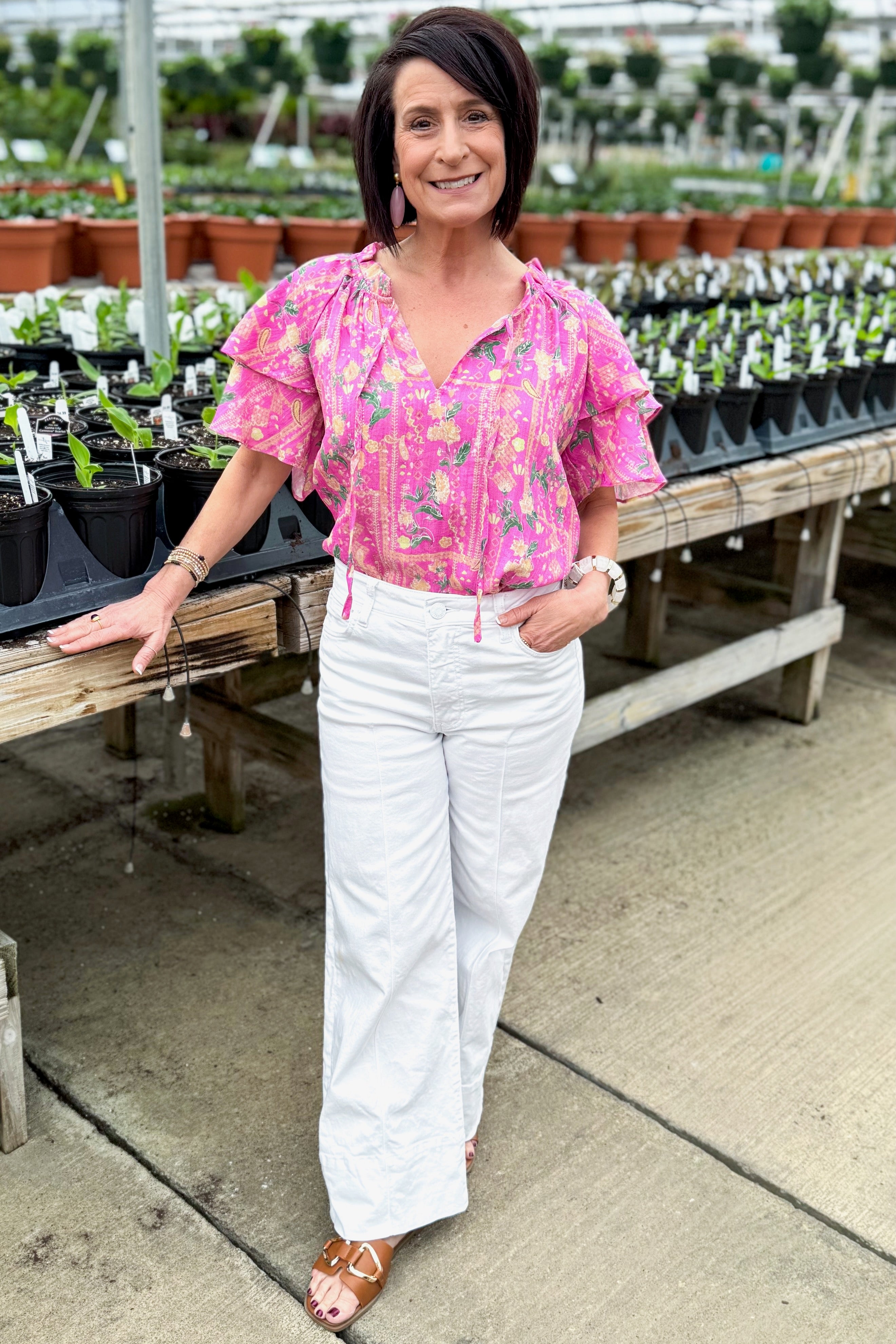 Front view of woman wearing Pink Floral Printed Ruffle Sleeve Top with jeans at a garden center.