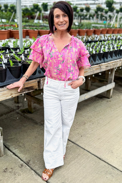 Front view of woman wearing Pink Floral Printed Ruffle Sleeve Top with jeans at a garden center.