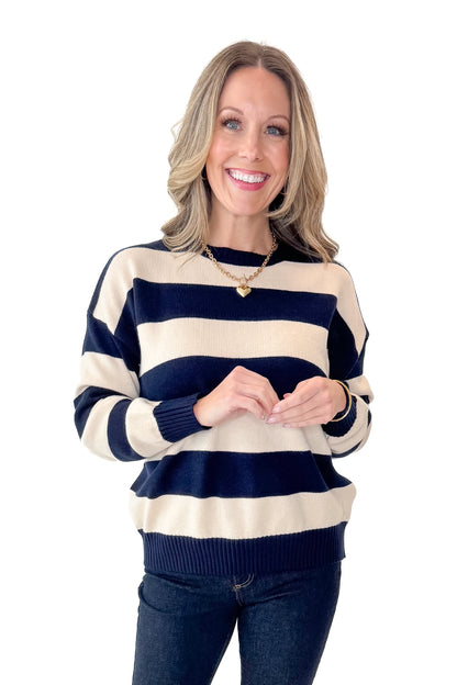 Front view of woman wearing Navy and Cream Striped Sweater with jeans against white studio background.