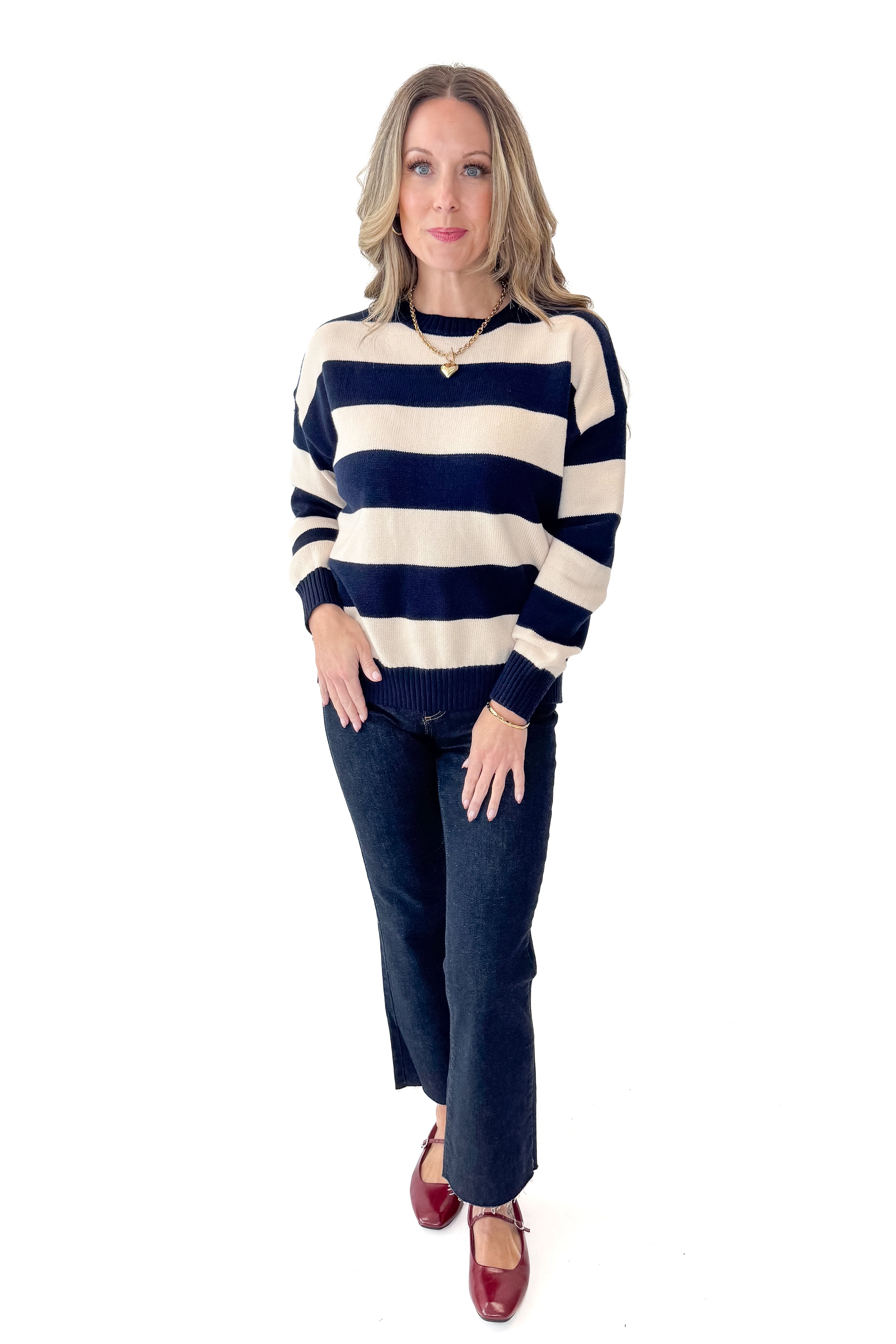 Front view of woman wearing Navy and Cream Striped Sweater with jeans against white studio background.