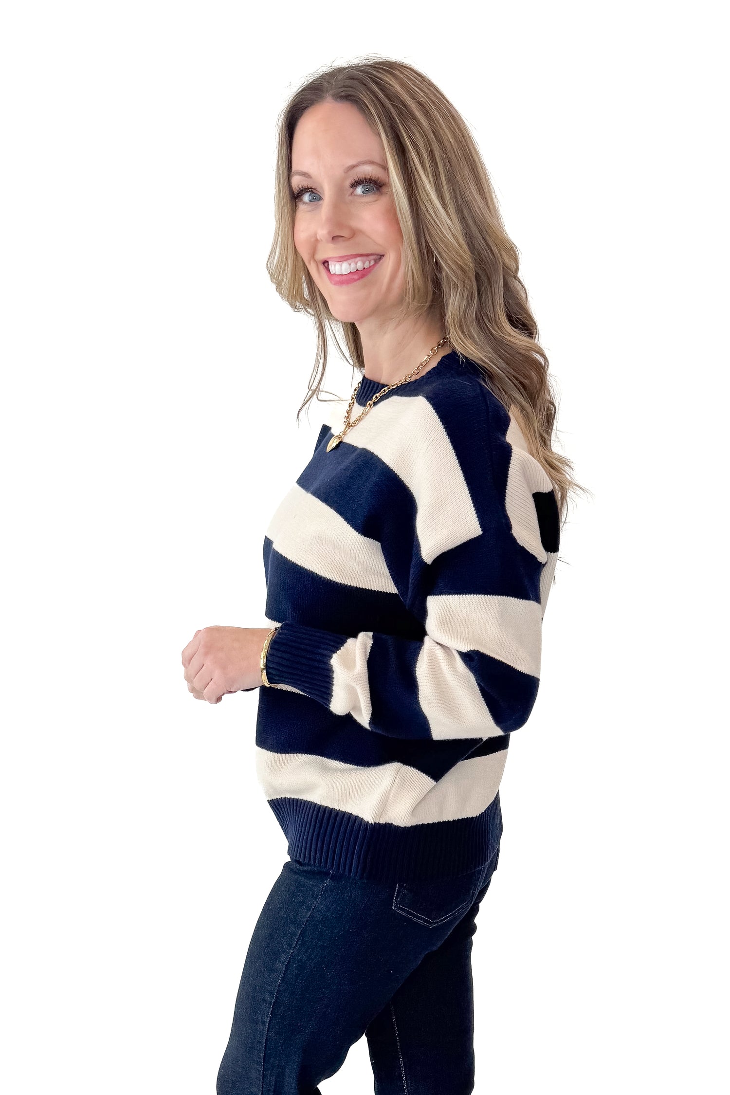 Side view of woman wearing Navy and Cream Striped Sweater with jeans against white studio background.