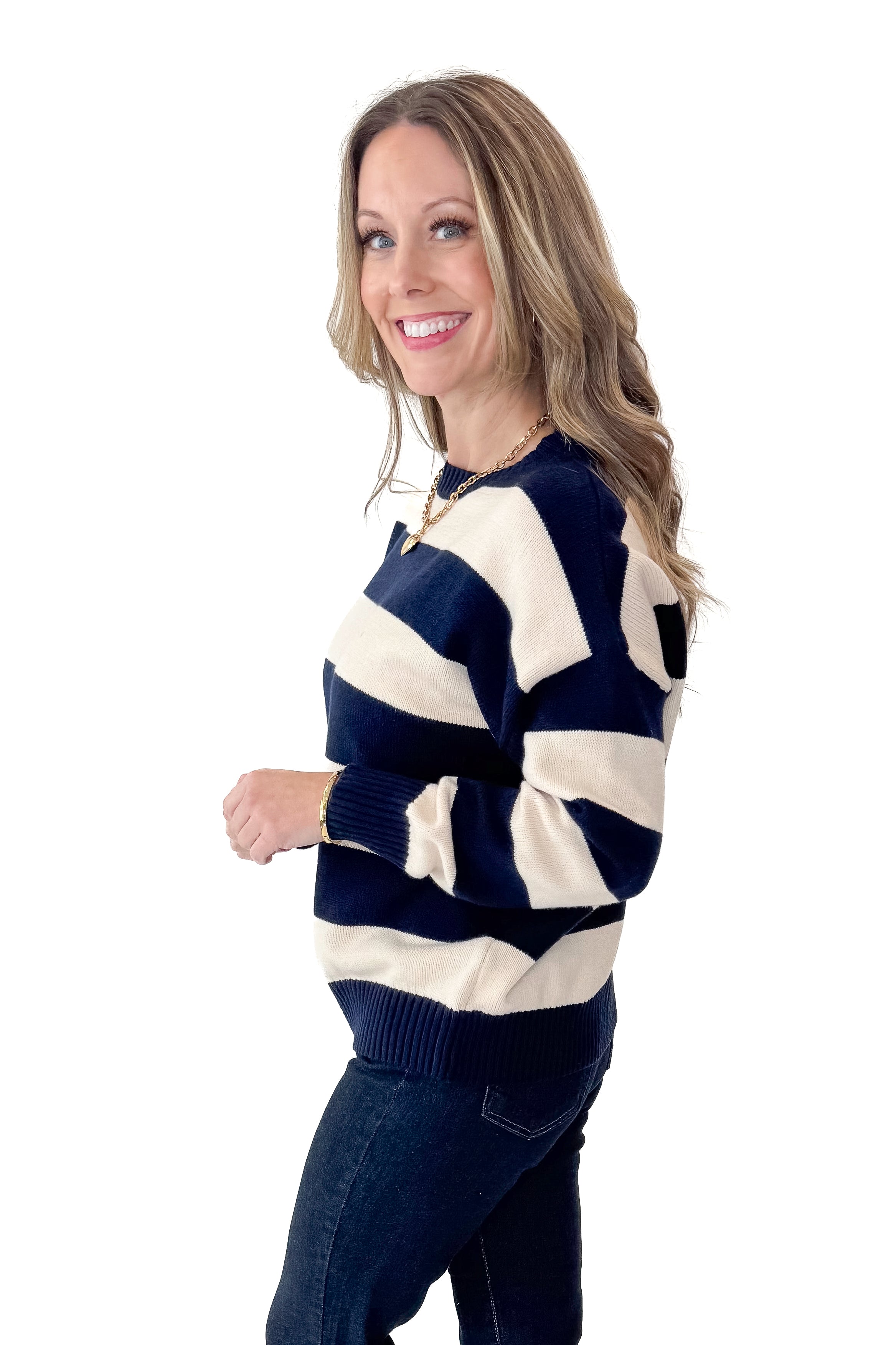 Side view of woman wearing Navy and Cream Striped Sweater with jeans against white studio background.