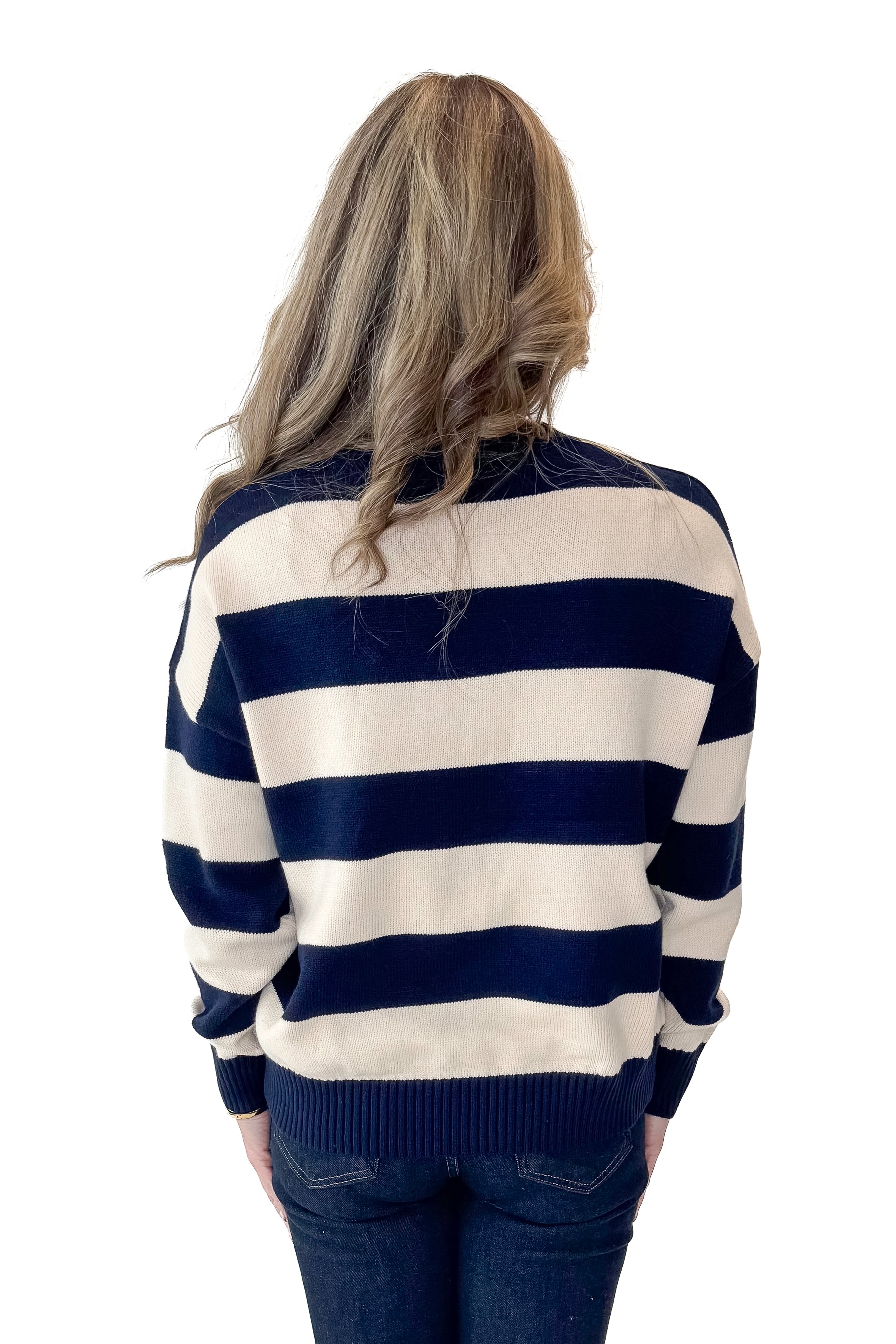 Back view of woman wearing Navy and Cream Striped Sweater with jeans against white studio background.