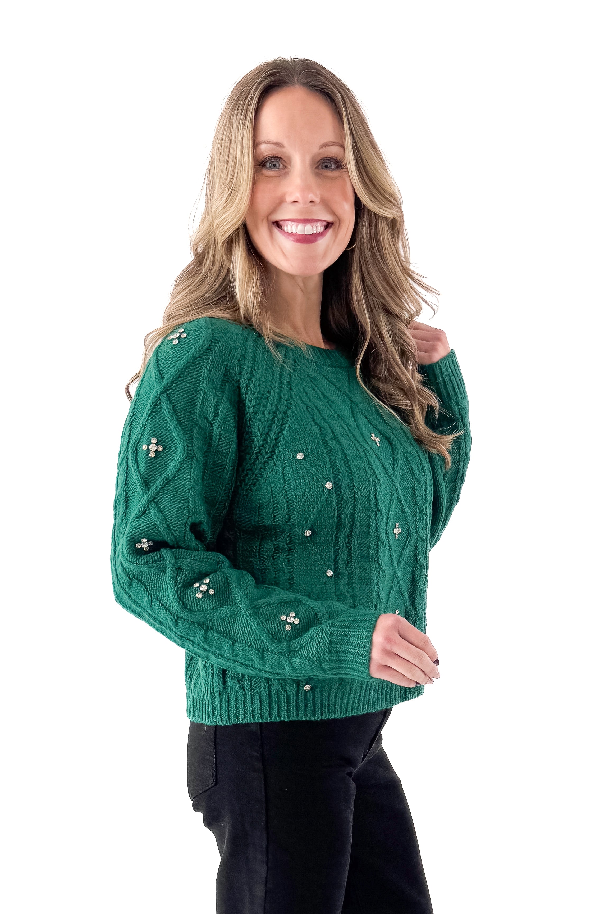 Side view of woman wearing Green Cable Knit Sweater With Rhinestones with jeans against white studio background.