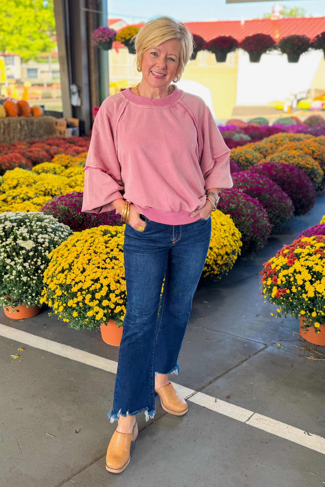 Woman outside wearing Washed Mauve Puff Sleeve Sweatshirt by She + Sky and jeans with mums in the background.