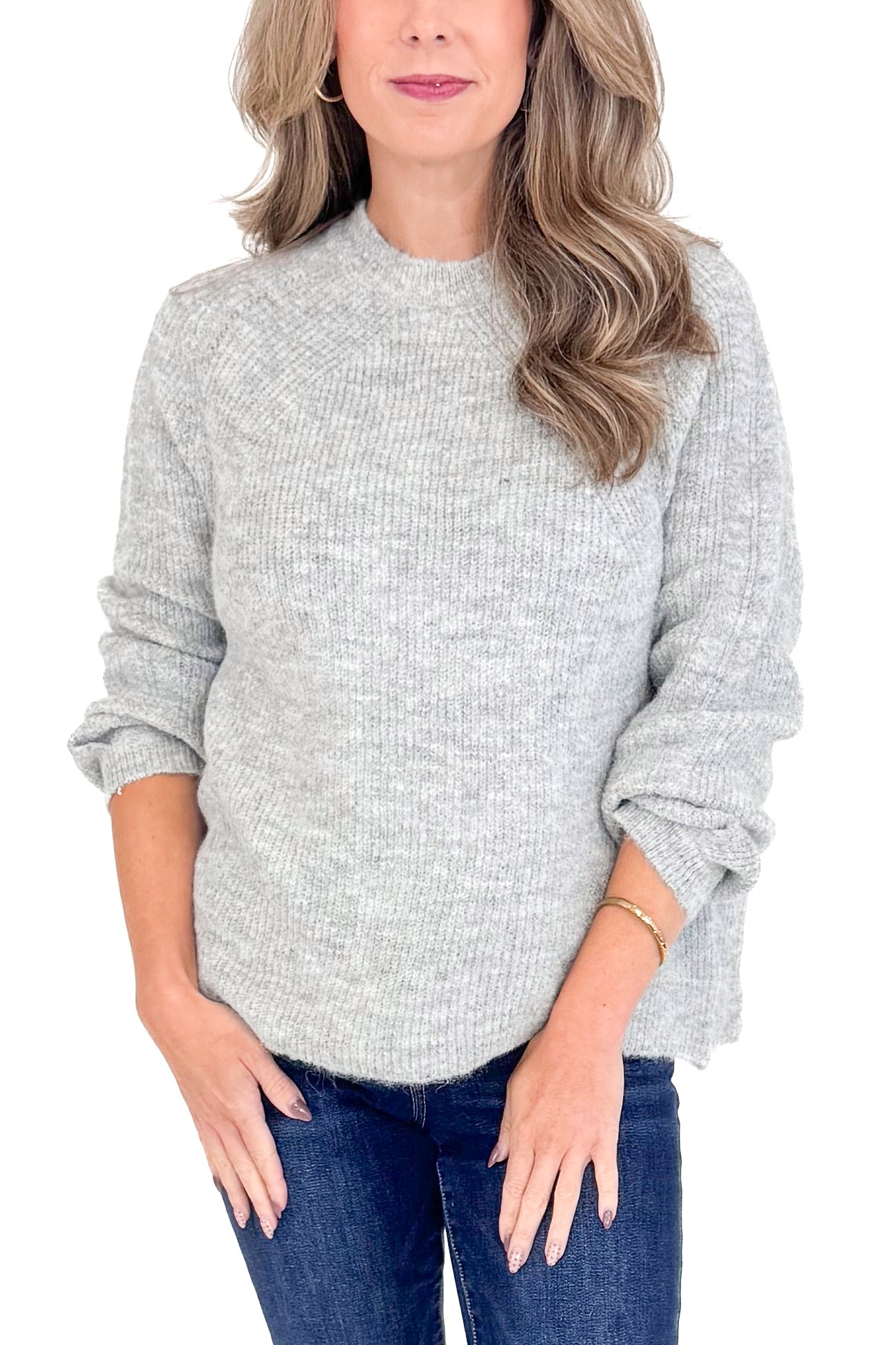 Front view of woman wearing grey ribbed sweater with jeans against white studio background.