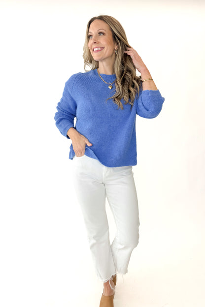 Front view of woman wearing Blue Ribbed Sweater with jeans against white studio background.