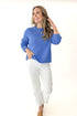 Front view of woman wearing Blue Ribbed Sweater with jeans against white studio background.