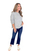 Front view of woman wearing grey ribbed sweater with jeans against white studio background.
