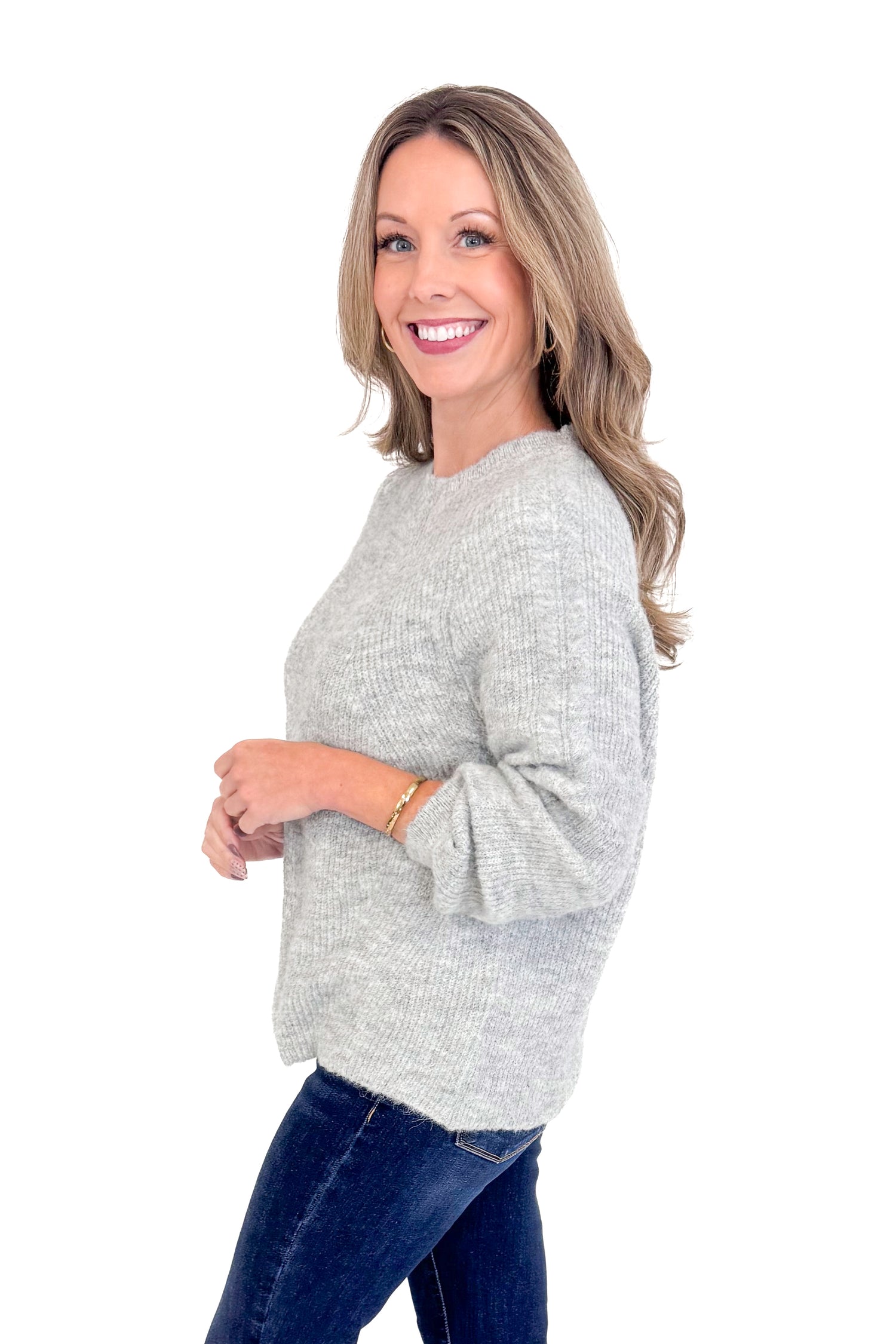 Side view of woman wearing grey ribbed sweater with jeans against white studio background.