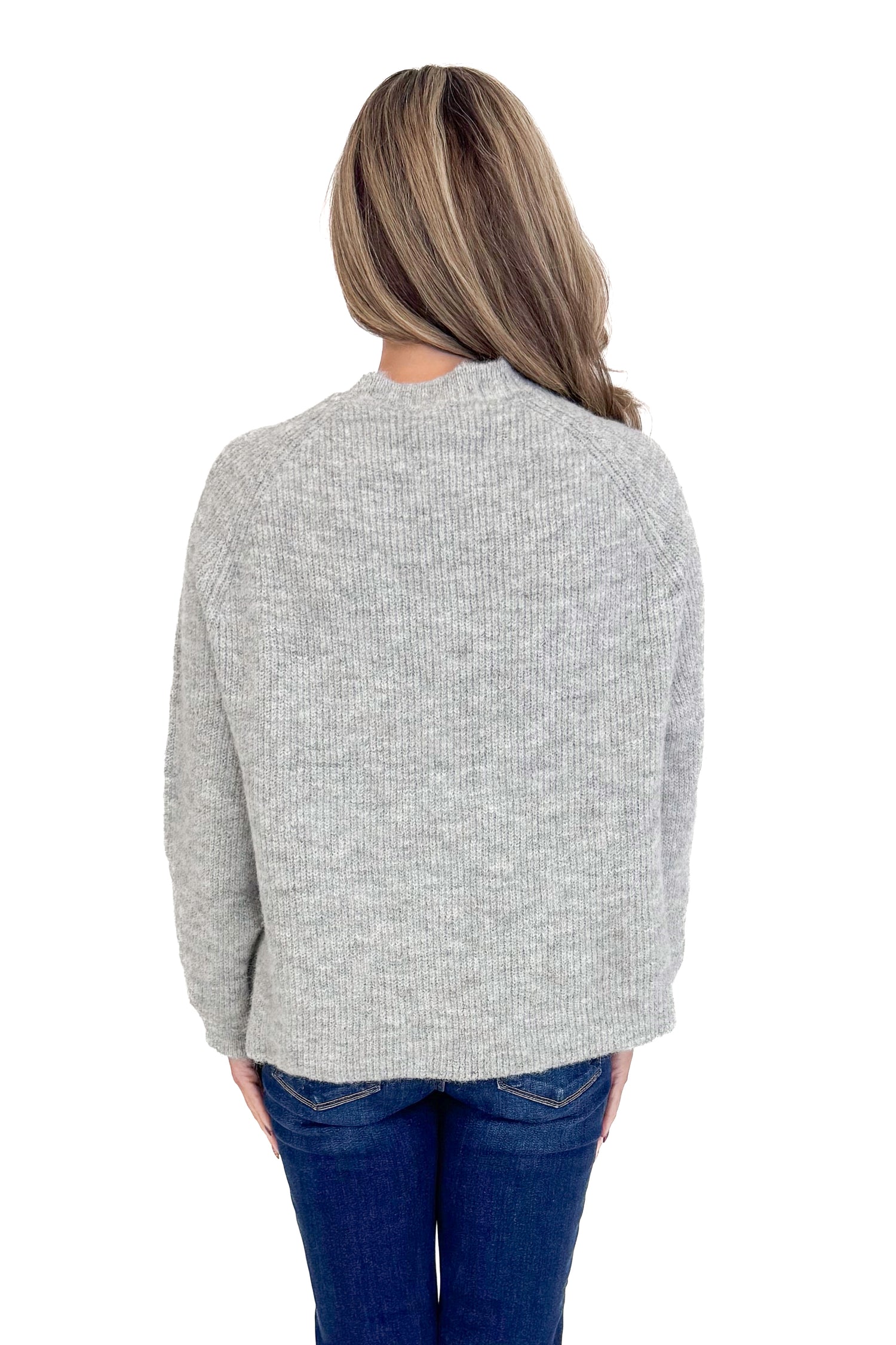 Back view of woman wearing grey ribbed sweater with jeans against white studio background.