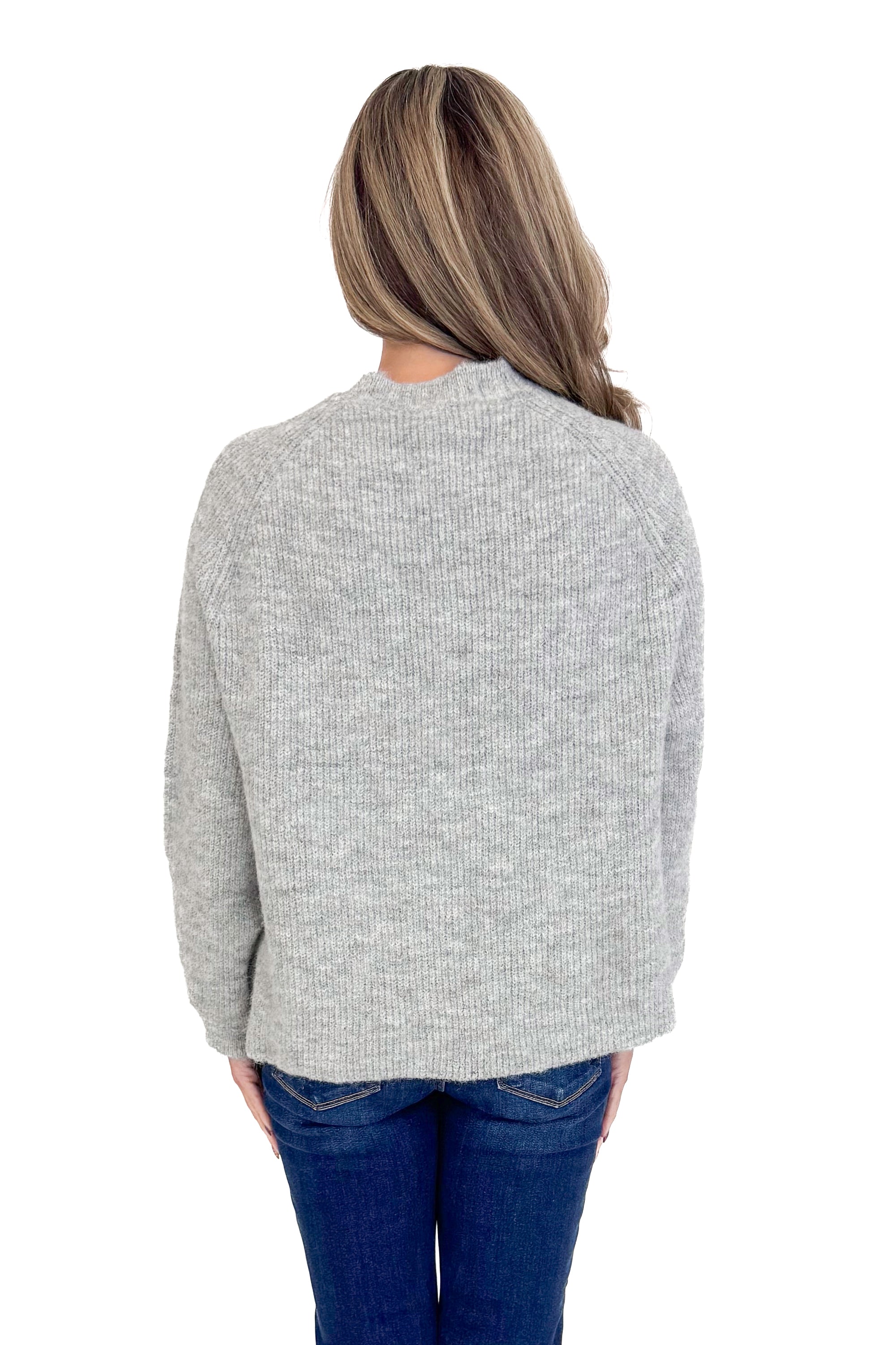 Back view of woman wearing grey ribbed sweater with jeans against white studio background.